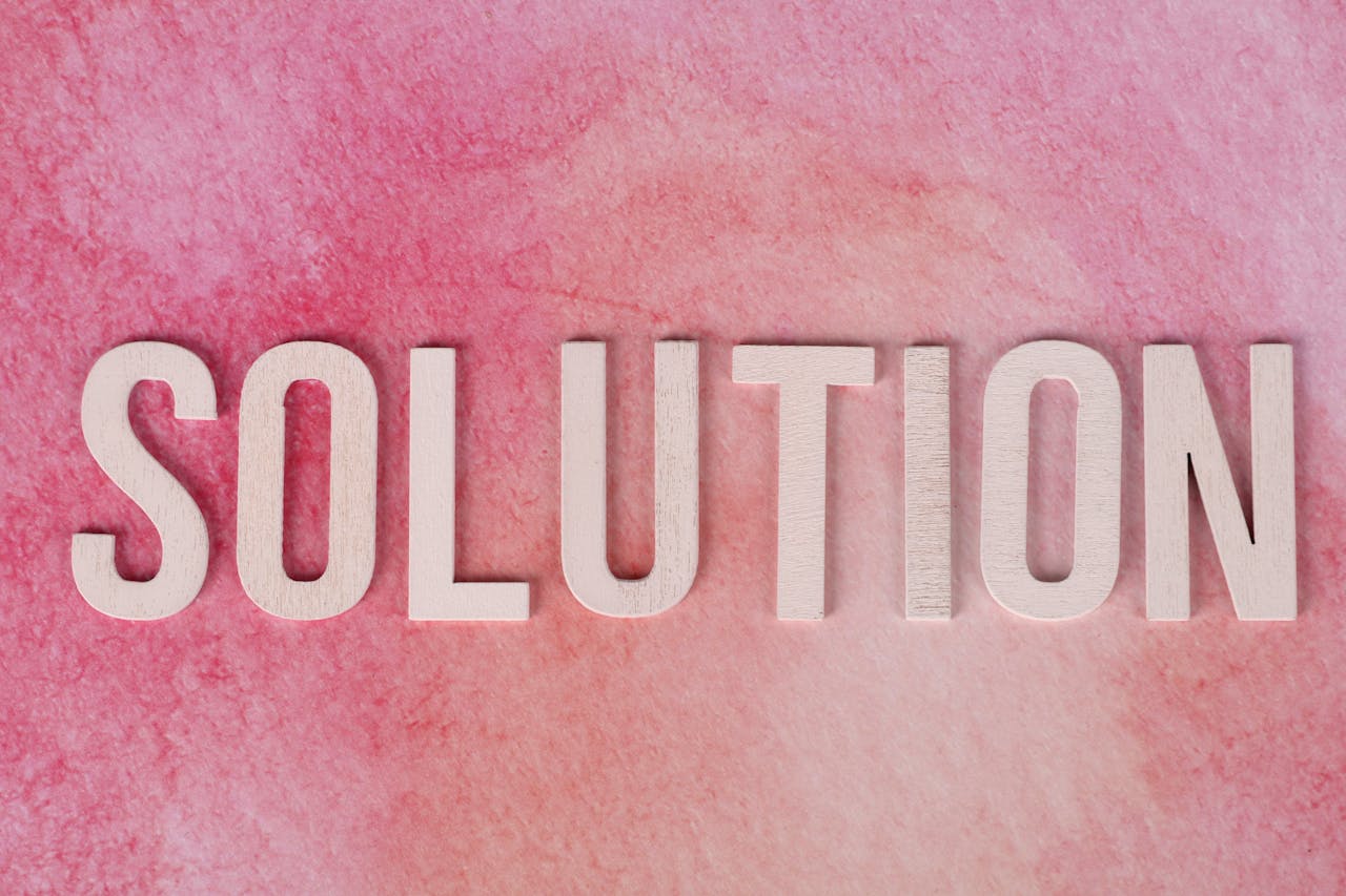 Wooden letters spelling Solution on a textured pink background.