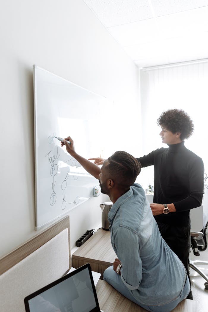 services-03 Two men brainstorming and collaborating at a whiteboard in a modern office setting.
